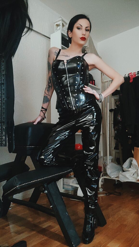 Very strict and dominant woman dressed in pvc leather corset and pants and wearing high heels, with beautiful face 