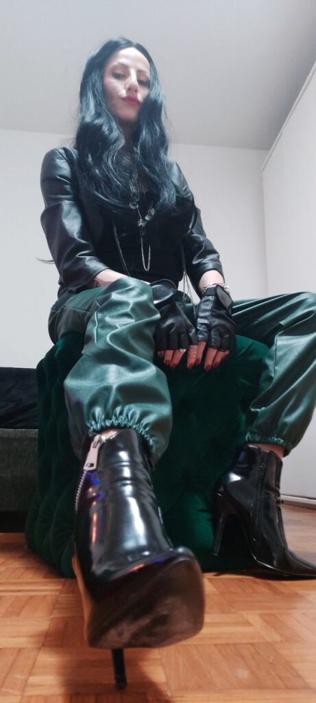 Dominant woman with long black hair dressed in leather with leather gloves and pvc heels